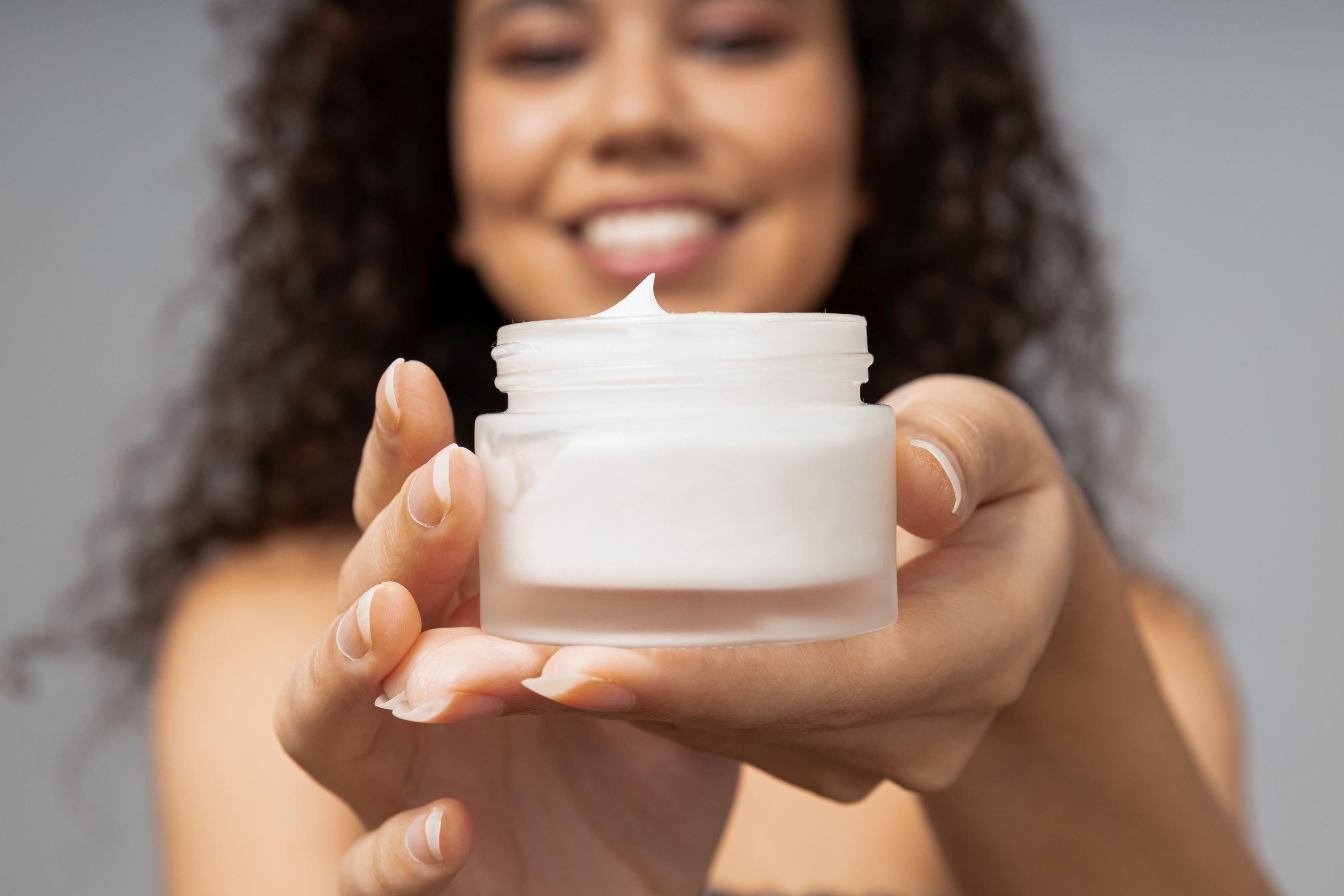 woman showing skin and face care cream hodling it with both hands in front of the screen